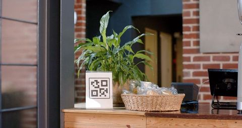 Qr code sign beside potted green plant on wooden counter with wicker basket and terminal