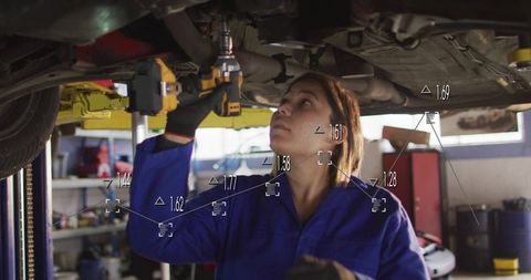 Woman mechanic tightening bolts under car using cordless impact wrench with data overlay