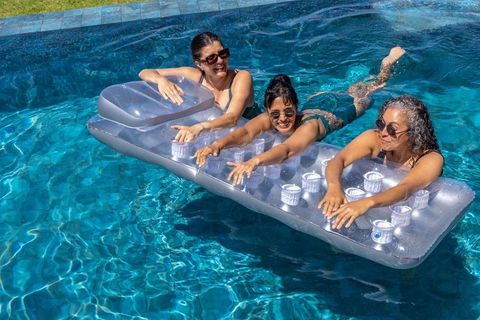 Three diverse mature women enjoying pool on clear inflatable lounger with cup holders