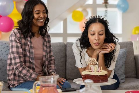 Young friends celebrating birthday on sofa blowing out candles with cake and balloons