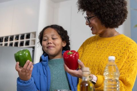 Diverse mother and daughter comparing green and red bell peppers during healthy meal prep
