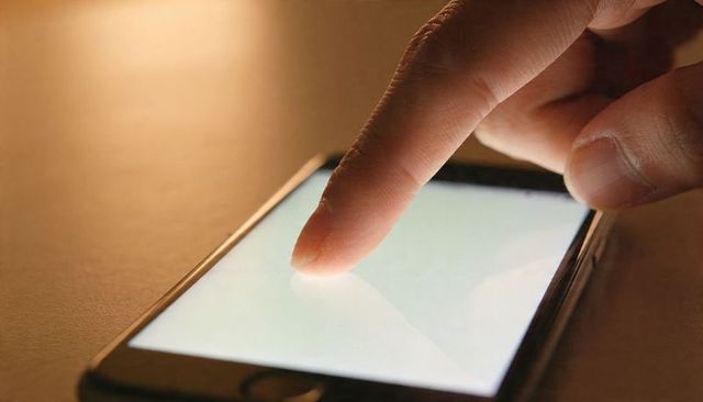 Index Finger Tapping Smartphone Touchscreen Showing Bright Touchpoint and Reflection on Desk