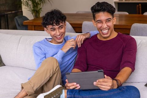 Joyful Friends Sitting on Sofa Utilizing Tablet Entertainment