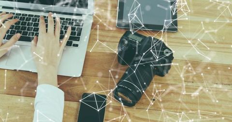 Typing woman working on laptop beside dslr camera and tablet with network overlay