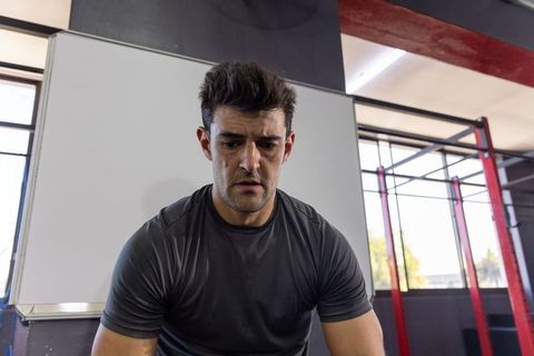 Tired male athlete resting between sets at gym whiteboard focused training and recovery