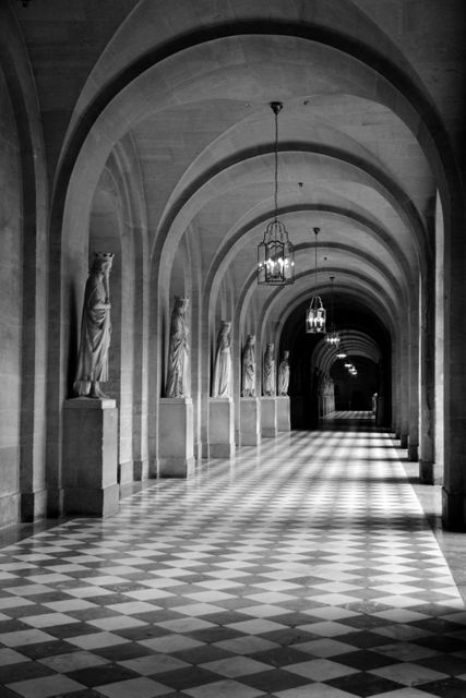 Black and white image showcasing a historic corridor with statues along the sides and arched ceilings. The checkerboard floor adds a vintage touch. Ideal for illustrating historic landmarks, architecture magazines, or art history content. Can be used for backgrounds in historical documentaries or museum displays.