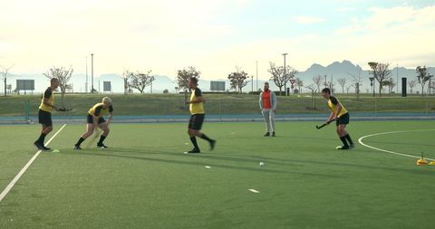 Male Field Hockey Team Practicing Pass Drills with Coach on Turf Field