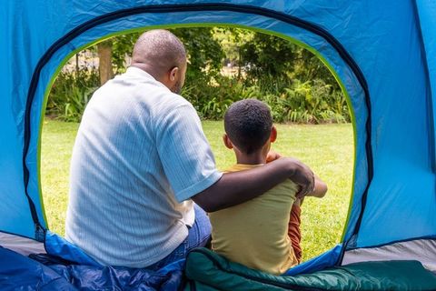 African american father embracing son while sitting in tent and overlooking green park