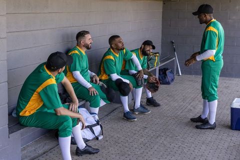 Baseball team gathering in dugout wearing green and yellow uniforms preparing for game