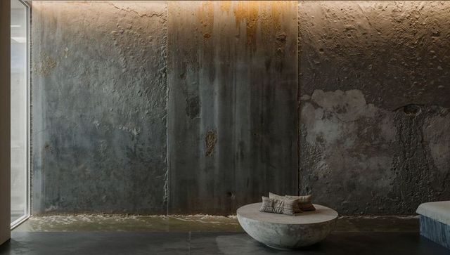 Minimalist concrete lobby with textured patina wall, wet strip and low round stone bench