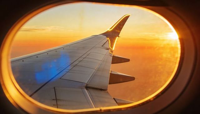 Golden sunset reflecting on airplane winglet through oval cabin window at dusk
