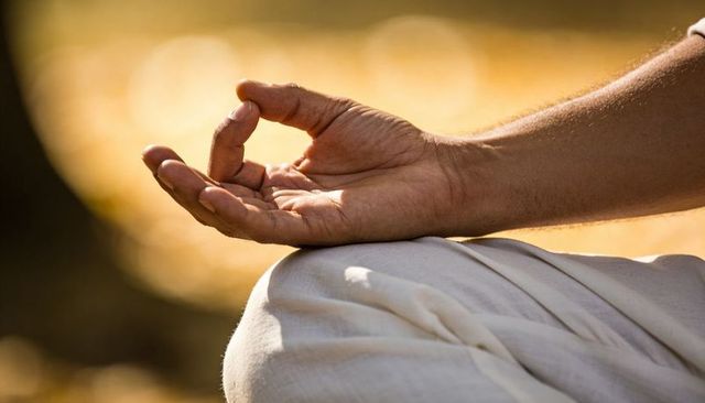 Right hand forming gyan mudra on knee during outdoor meditation in golden sunlight