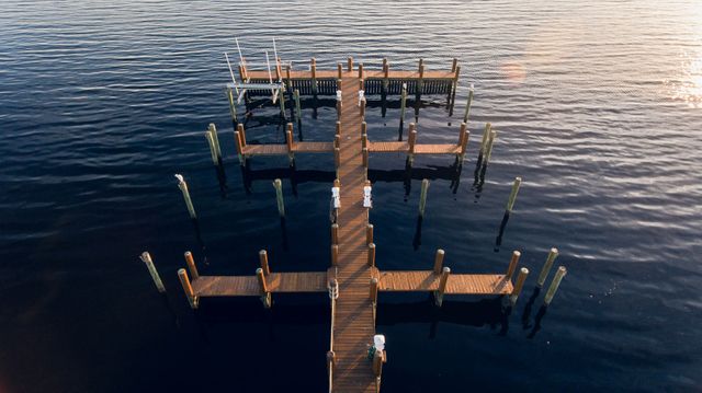 Wooden dock extending into calm water during sunset reflects peaceful and serene atmosphere. Ideal for travel, relaxation, nature, and vacation themes.