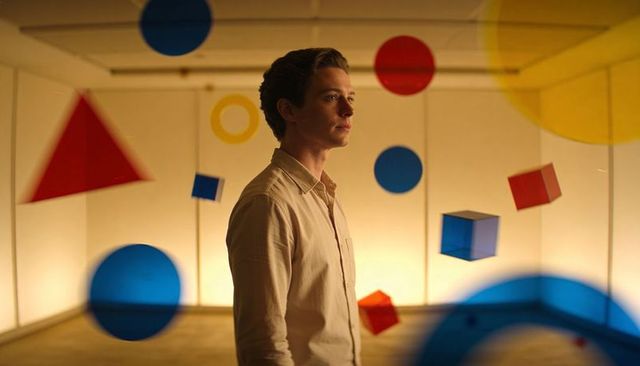 Man standing among suspended colorful geometric shapes in minimalist art installation