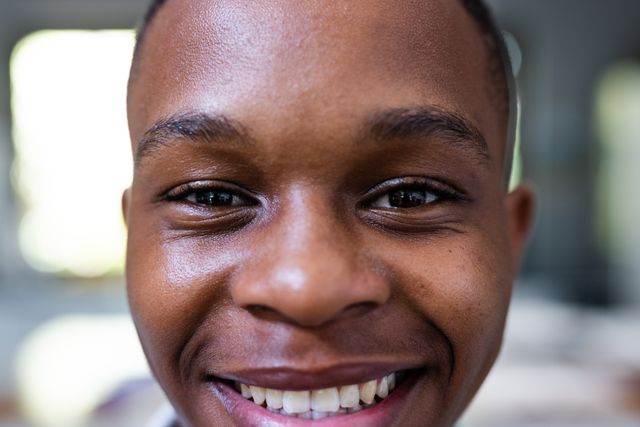This image captures a close-up of a smiling African American teenage boy, showcasing his happiness and youthful energy. Ideal for use in campaigns promoting youth positivity, lifestyle blogs, educational materials, and advertisements targeting teenagers. The image conveys a sense of joy and optimism, making it suitable for various contexts where a positive and cheerful representation of adolescence is needed.
