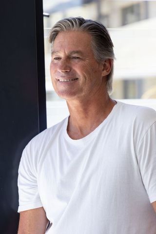 Mature man smiling and leaning on glass balcony railing in white t-shirt