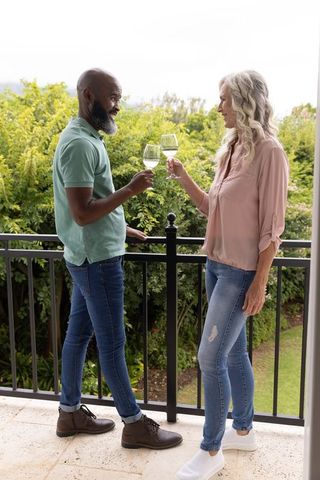Interracial mature couple toasting with wine on balcony, enjoying outdoor moment
