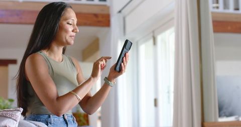 African american woman using smartphone in bright modern living room with loft style