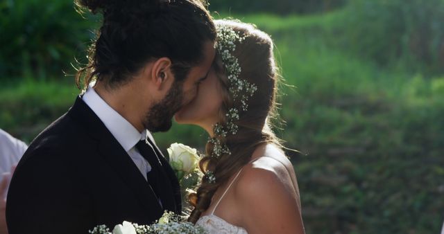 A young Caucasian couple shares a kiss on their wedding day, with copy space. Dressed in formal attire, the bride and groom's intimate moment is captured amidst a natural backdrop, symbolizing the beginning of their life together.