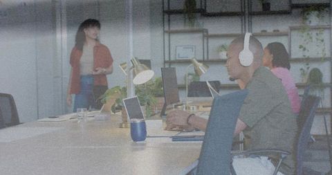 Focused coworking team typing on laptops wearing over-ear headphones in modern green workspace