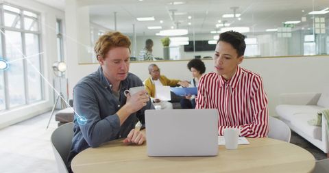 Collaborative Workplace with Diverse Professionals Discussing Over Laptop