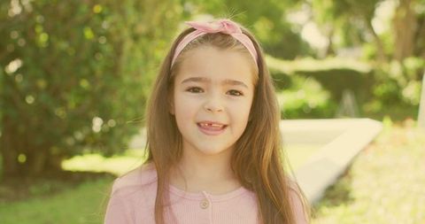 Smiling Little Girl Showing Missing Front Tooth in Sunlit Garden Wearing Pink Headband