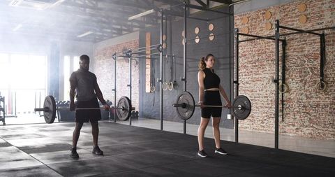 Diverse training partners lifting barbells in industrial gym