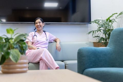 Smiling nurse in pink scrubs relaxing in contemporary staff lounge with greenery