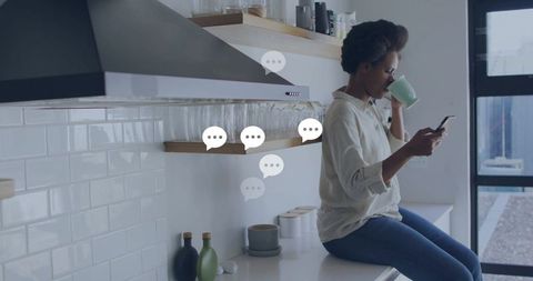 Morning messaging woman sipping green mug checking smartphone on modern minimalist kitchen counter