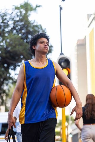 African american young basketball player walking urban street carrying ball and duffel bag