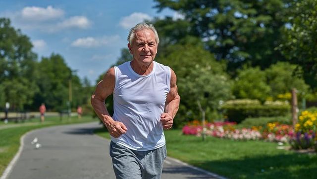 Senior man jogging through sunny park path passing flowerbeds and birds, healthy lifestyle