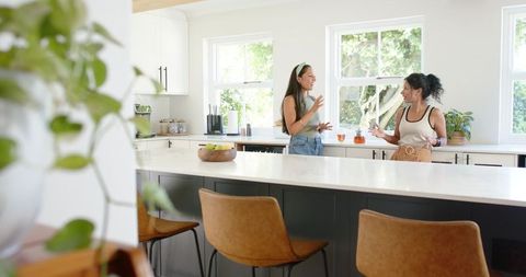 Friends chatting at bright modern kitchen island holding drinks, casual home gathering