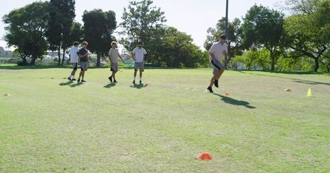 Male teammates running agility drill on grass field with colored cones for coaching and fitness