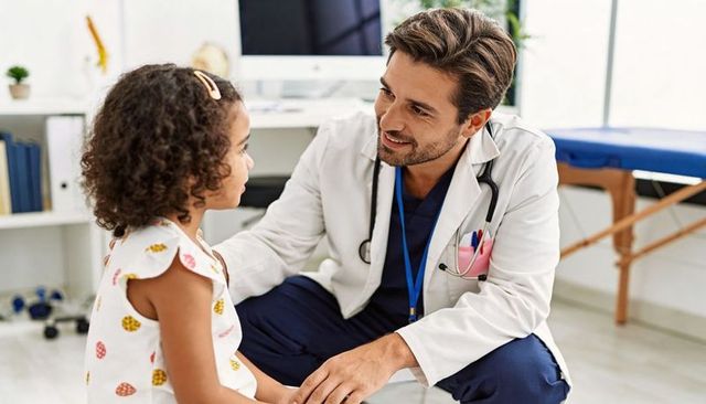 Pediatrician kneeling and comforting child, smiling and building trust in bright clinic