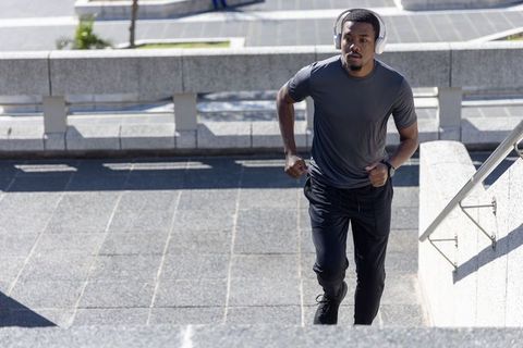 African American man running stairs during urban workout wearing headphones and tracker