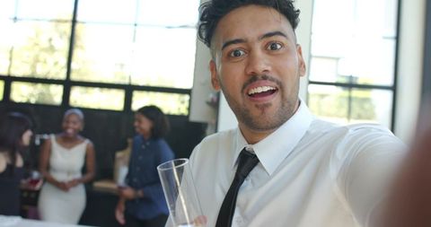 Young professional taking selfie at networking reception while holding champagne glass
