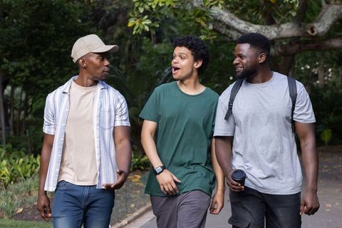 Three african american friends walking and talking in park casual conversation and laughter