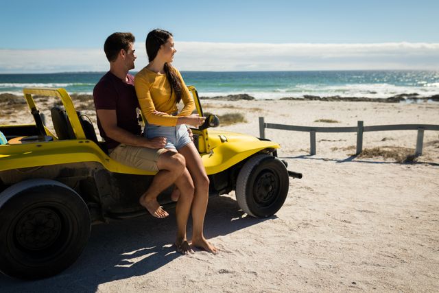 Couple sitting on a yellow beach buggy, embracing and admiring the ocean view. Ideal for travel and tourism promotions, romantic getaway advertisements, and lifestyle blogs focusing on summer adventures and road trips.