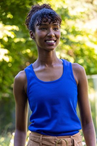 Smiling african american woman wearing royal blue tank and belted shorts in sunlit park