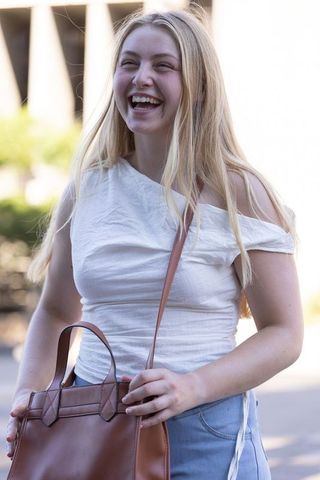 Blonde woman laughing while holding brown leather crossbody bag on city street