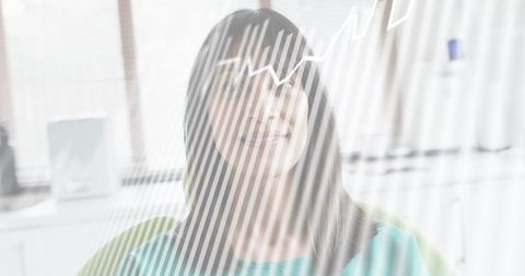 Professional woman wearing glasses sitting in bright office, gazing through striped blinds