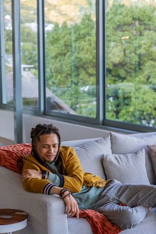 Relaxed african american man reclining on sofa showing smartwatch in bright living room