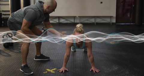 Coach guiding female athlete holding plank in gym for core strength and proper form