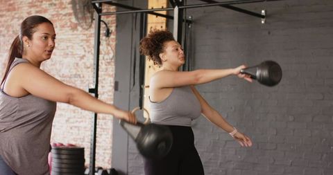 Diverse women performing kettlebell swings in urban fitness studio partner training