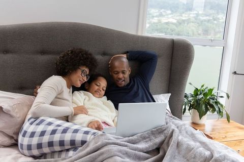 Cozy family cuddling in bed watching laptop together under sunlit window morning routine