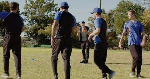 Coach guiding youth team during outdoor training drill with blue uniforms and cone