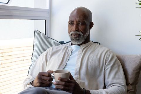 Senior african american man holding mug and relaxing on sunlit minimalist sofa