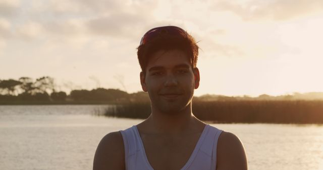 Young man standing near a calm lake during sunset, soft light creating a serene mood, suitable for promoting outdoor activities, relaxation, or lifestyle content.
