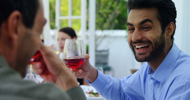 A middle-aged Middle Eastern man is smiling and toasting with a glass of wine during an outdoor gathering, with copy space. His joyful expression and the social setting suggest a celebration or a casual get-together with friends or family.