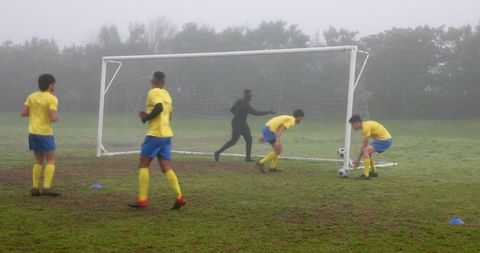Soccer Players Training with Coach on Misty Field Preparing for Match